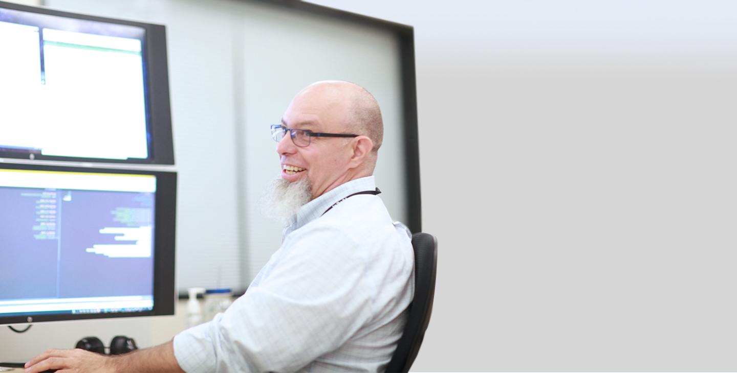 Viasat government service team member shitting at a computer looking over his shoulder and smiling